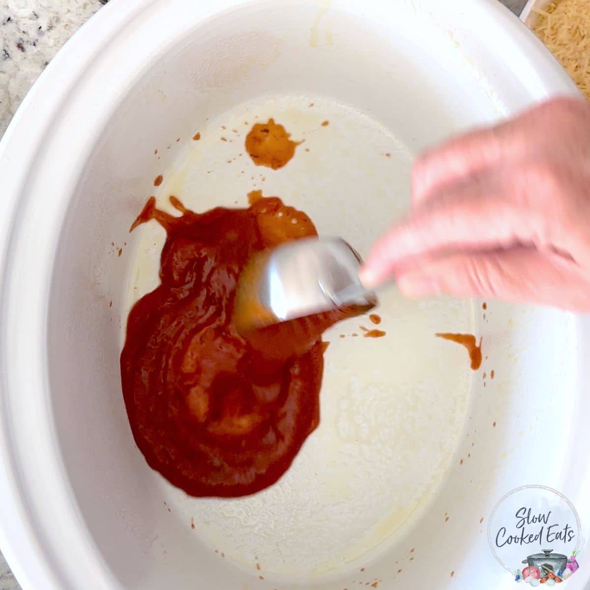 Pouring marinara sauce into the bottom of a greased crockpot.