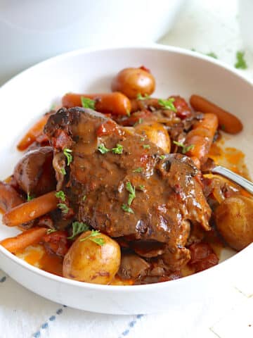 Slow cooker beef roast in a white bowl garnished with fresh parsley.