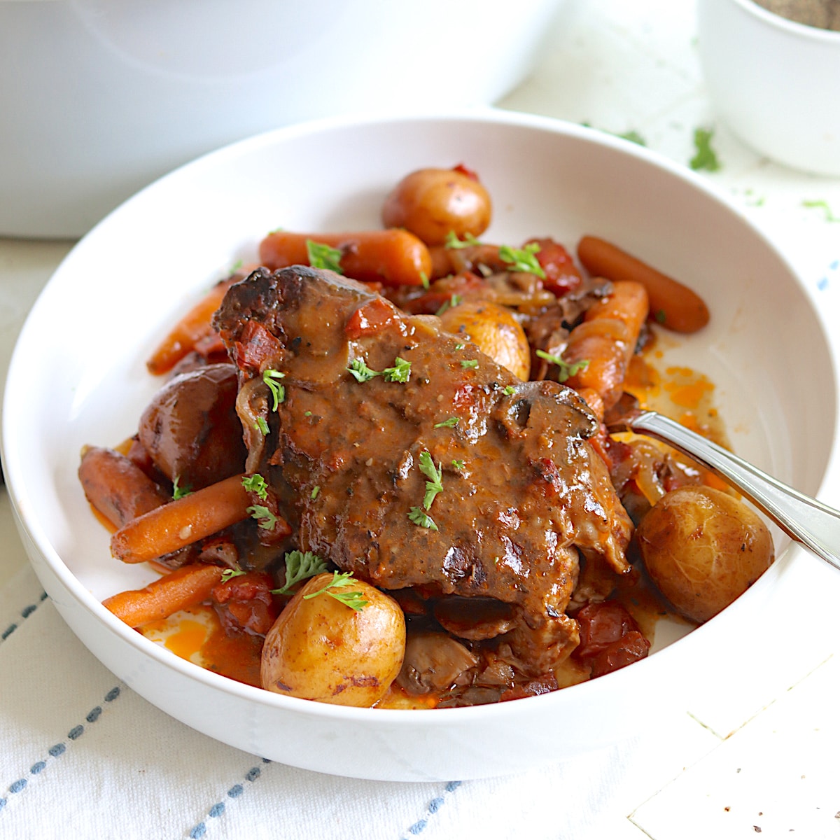 Slow cooker beef roast in a white bowl garnished with fresh parsley.