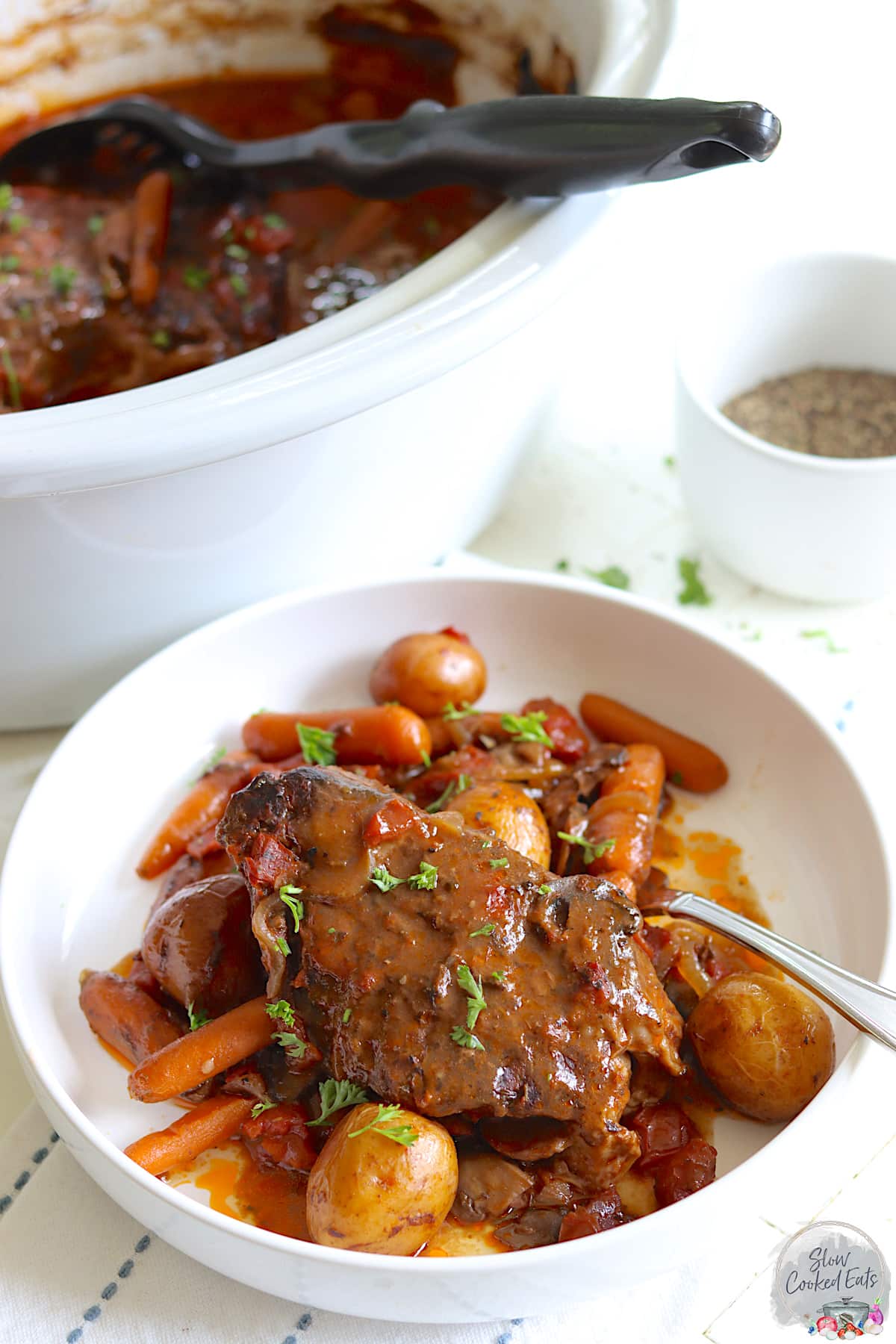 Crockpot pot roast served over carrots, potatoes, and mushrooms in a white bowl.