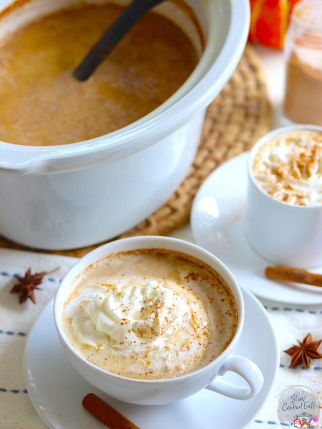 crockpot pumpkin spice latte served in a white cup and saucer with a cinnamon stick and dollop of whipped cream.