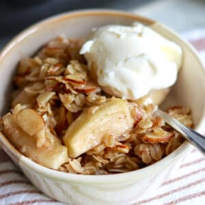 A single serving of slow cooker apple crisp with crumble topping and vanilla ice cream