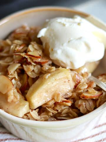 A single serving of slow cooker apple crisp with crumble topping and vanilla ice cream