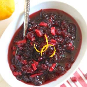A white bowl with crockpot cranberry sauce topped with orange zest on a red and white striped napkin.
