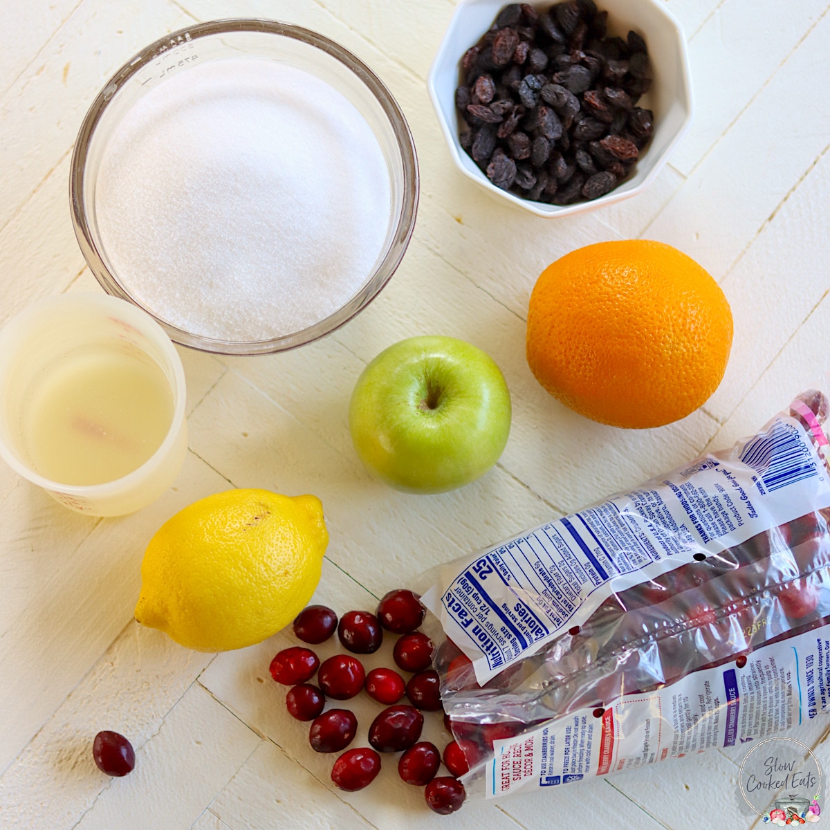 Ingredients needed for making crockpot cranberry sauce on a white wood board.