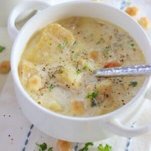 Slow cooker fish chowder in a white handled bowl with fresh parsley and oyster crackers.
