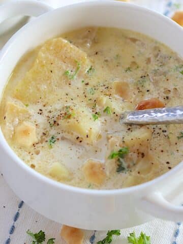 Slow cooker fish chowder in a white handled bowl with fresh parsley and oyster crackers.