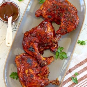 Crockpot BBQ chicken quarters arranged on a gray platter with fresh parsley.