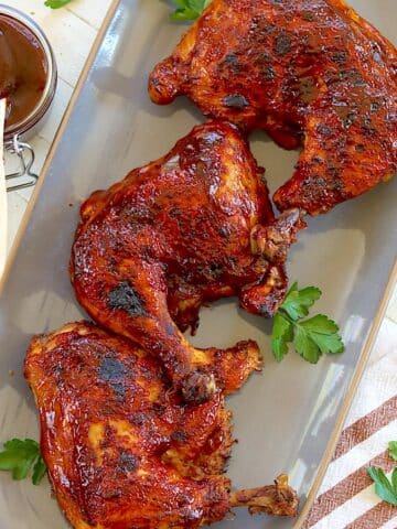 Crockpot BBQ chicken quarters arranged on a gray platter with fresh parsley.