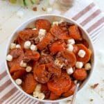 Crockpot candied sweet potatoes in a white bowl sprinkled with mashmallows and cinnamon.