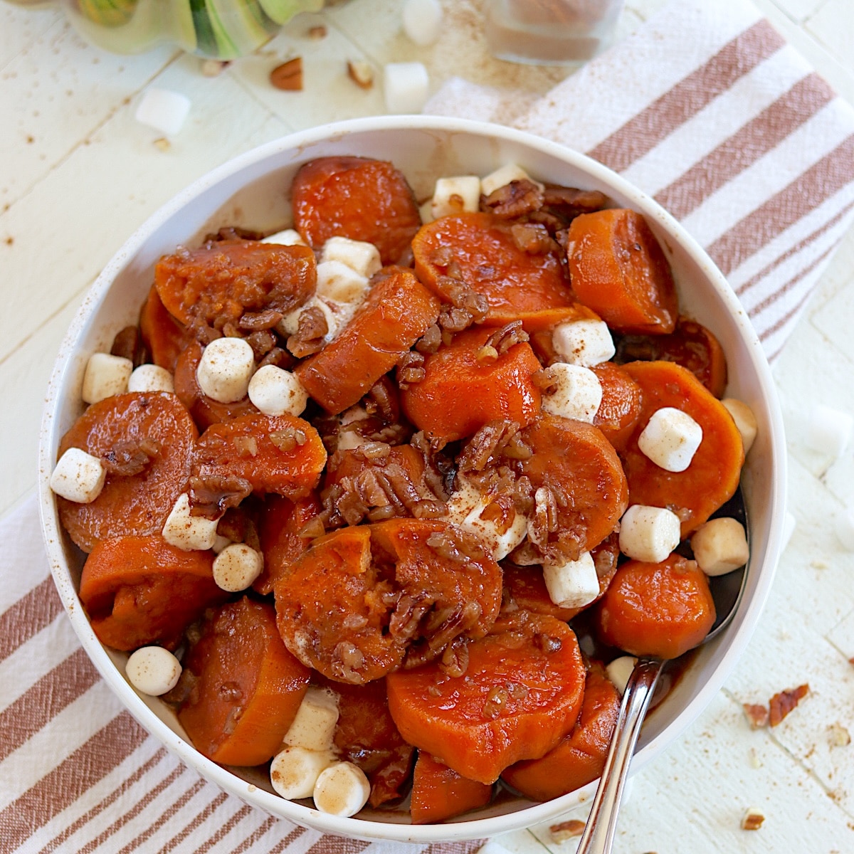 Crockpot candied sweet potatoes in a white bowl sprinkled with mashmallows and cinnamon.
