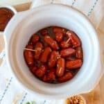 Crockpot little smokies in a white slow cooker sprinkled with brown sugar.