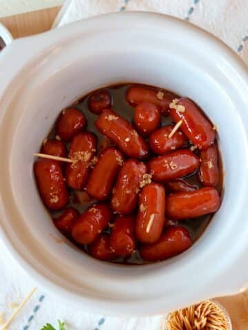 Crockpot little smokies in a white slow cooker sprinkled with brown sugar.