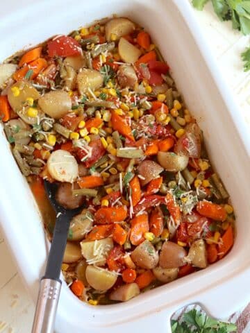 Slow cooker vegetables in a white rectangle crock garnished with parsley and parmesan cheese.