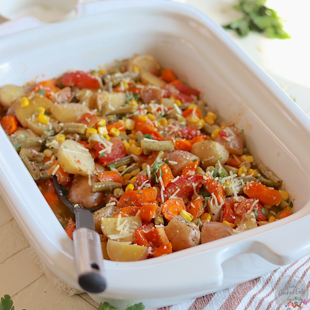 A white rectangle crockpot with mixed slow cooker vegetables garnished with parmesan cheese.
