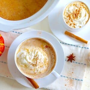 Crockpot pumpkin spice latte in two white cups and saucers with whipped cream and cinnamon.