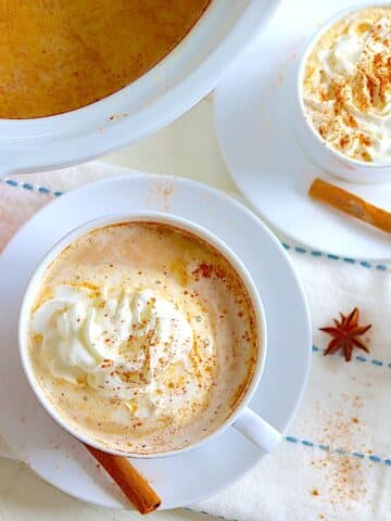 Crockpot pumpkin spice latte in two white cups and saucers with whipped cream and cinnamon.