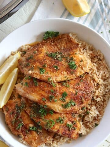 A white bowl with rice and four crockpot tilapia fillets with lemon wedges.