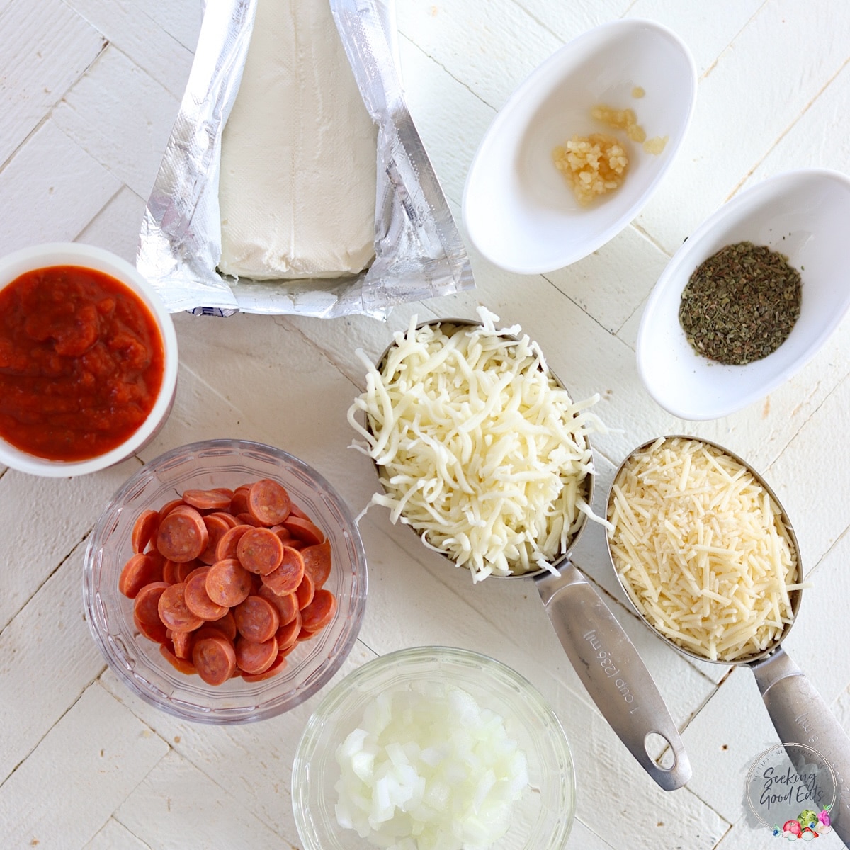 Ingredients needed for making crockpot pizza dip on a white wooded board.