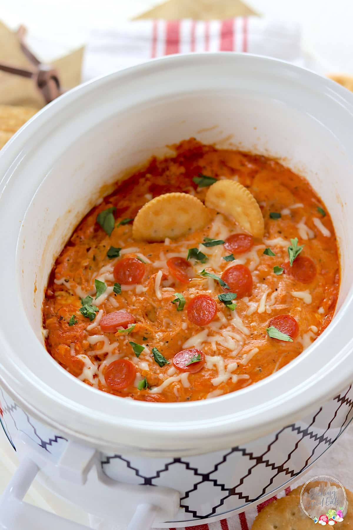 Crock Pot Pizza Dip in a white oval slow cooker with crackers for serving.
