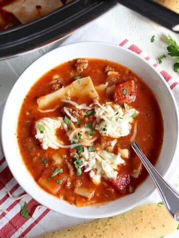 Cheesy slow cooker lasagna soup served in a white bowl with a spoon and garnished with fresh parsley.