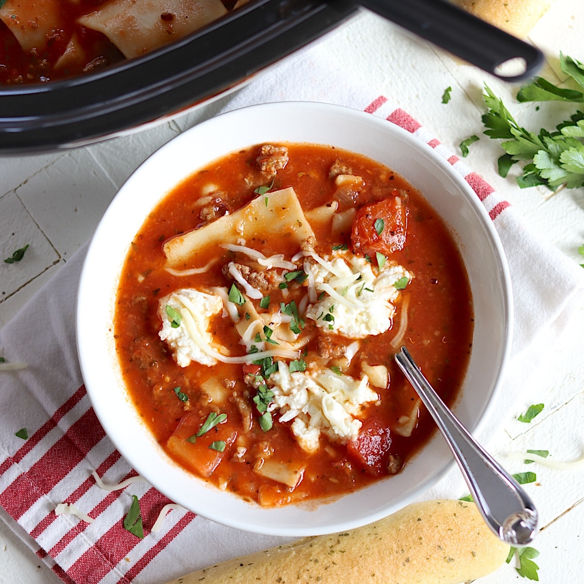 Cheesy slow cooker lasagna soup served in a white bowl with a spoon and garnished with fresh parsley.