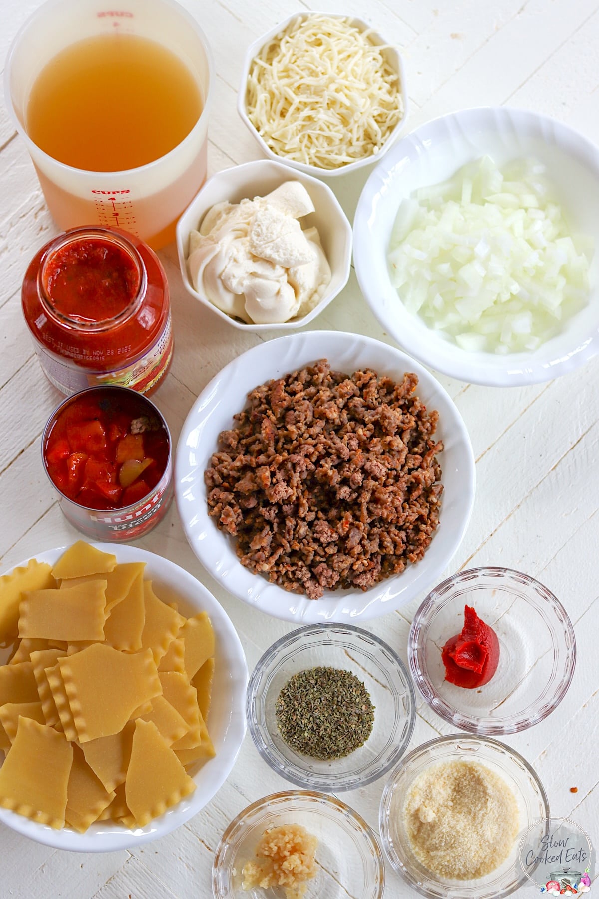 Ingredients needed for making slow cooker lasagna soup on a white wooden board.