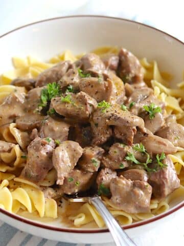 A brown rimmed white bowl with slow cooker beef stroganoff served over egg noodles.