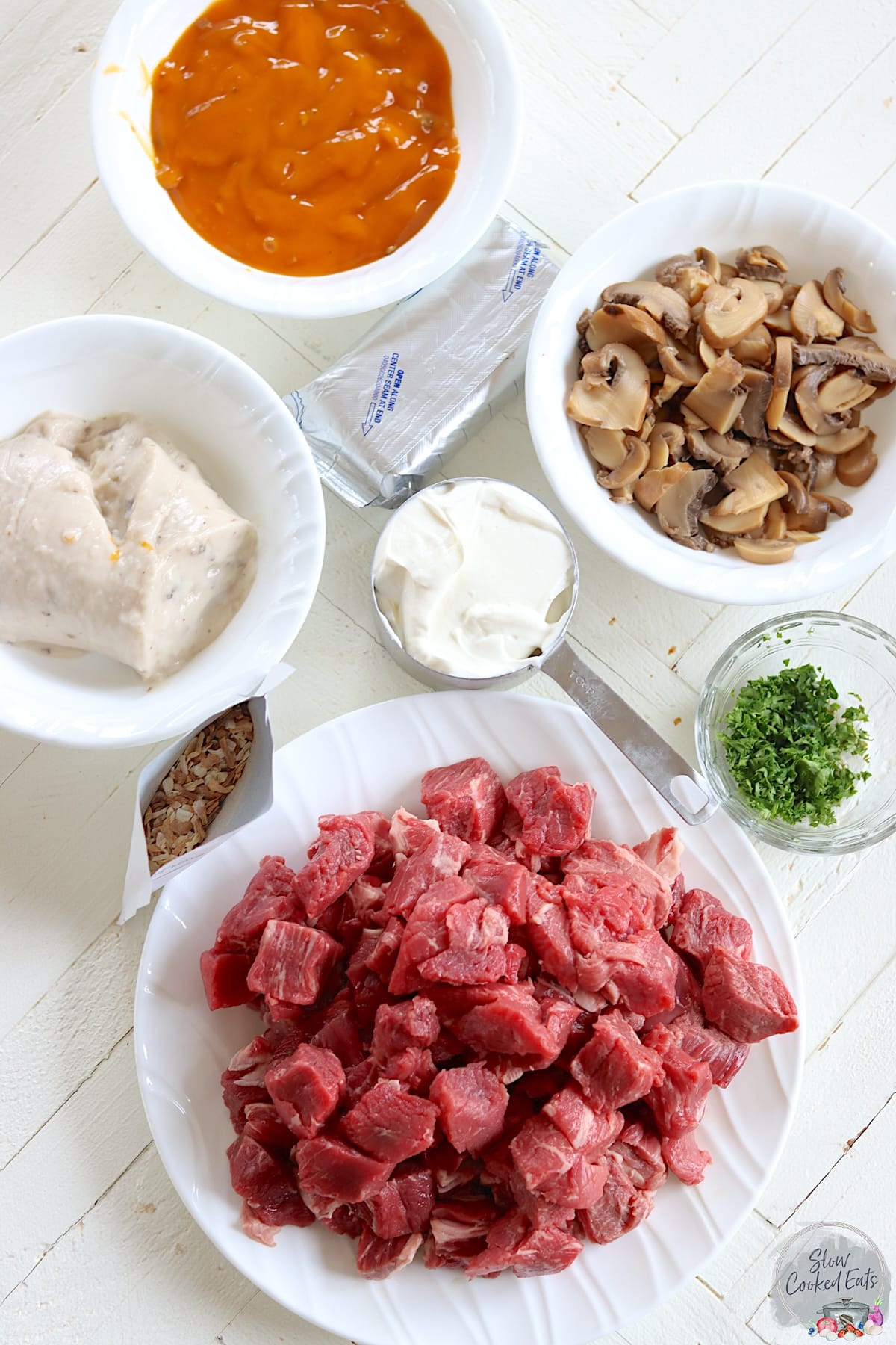 Ingredients needed to make crock pot beef stroganoff on a white wooden board.