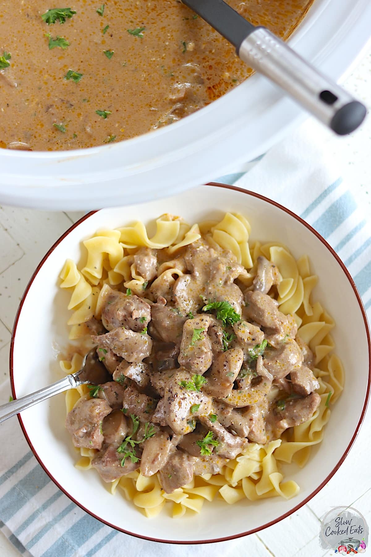 A white bowl with brown edge served with slow cooker beef stroganoff over egg noodles.