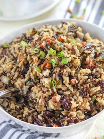 Crockpot brown rice pilaf served in a white bowl and garnished with pecans and green onion.