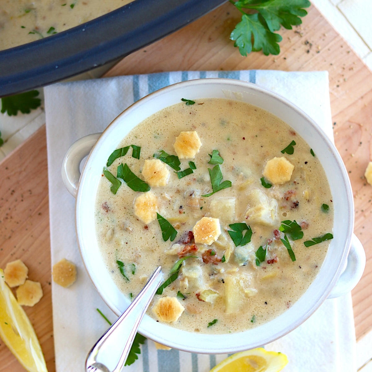 Crockpot clam chowder served in a white bowl with crackers and fresh parsley.