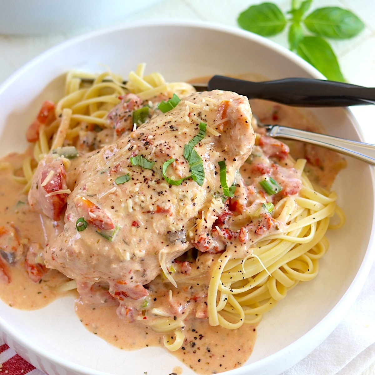 Crockpot marry me chicken over pasta in a white bowl and garnished with fresh basil and parmesan cheese.