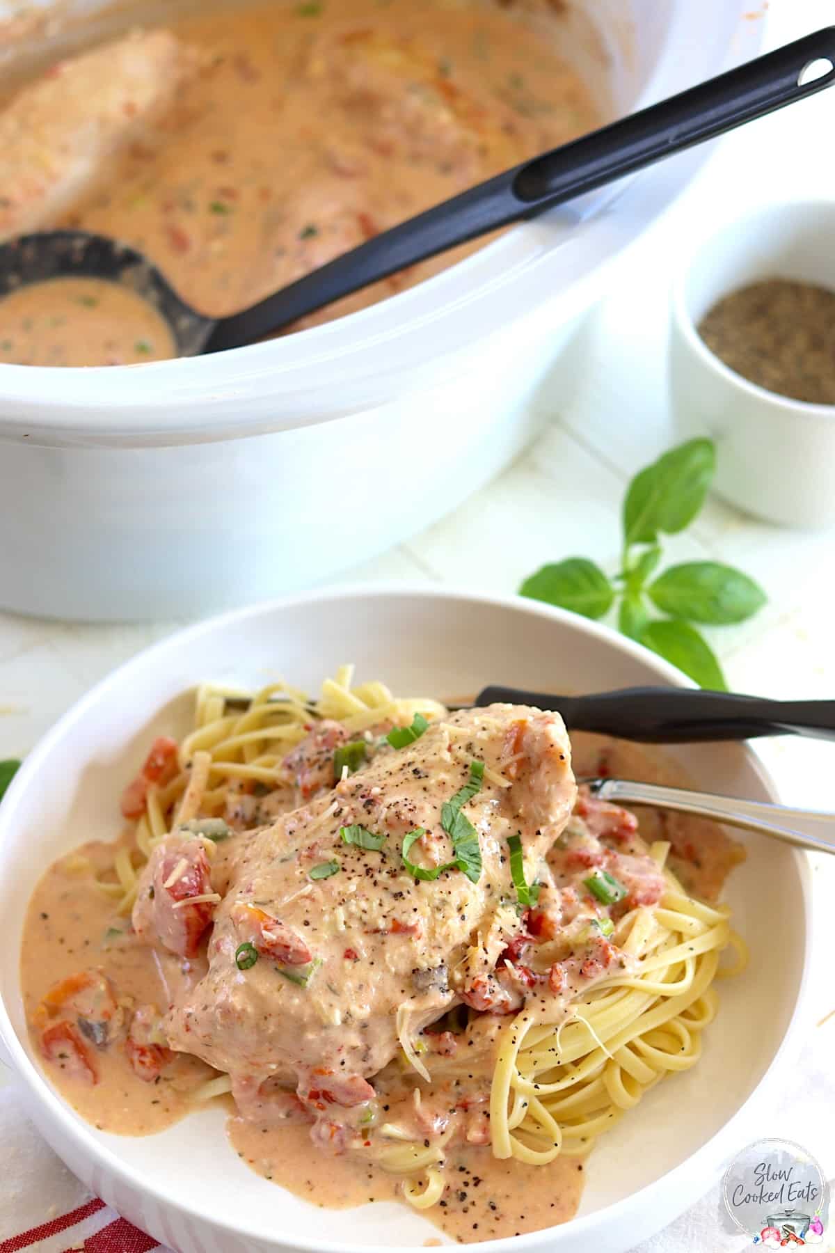 A white crock pot and plate with marry me chicken crock pot recipe served over linguine noodles.