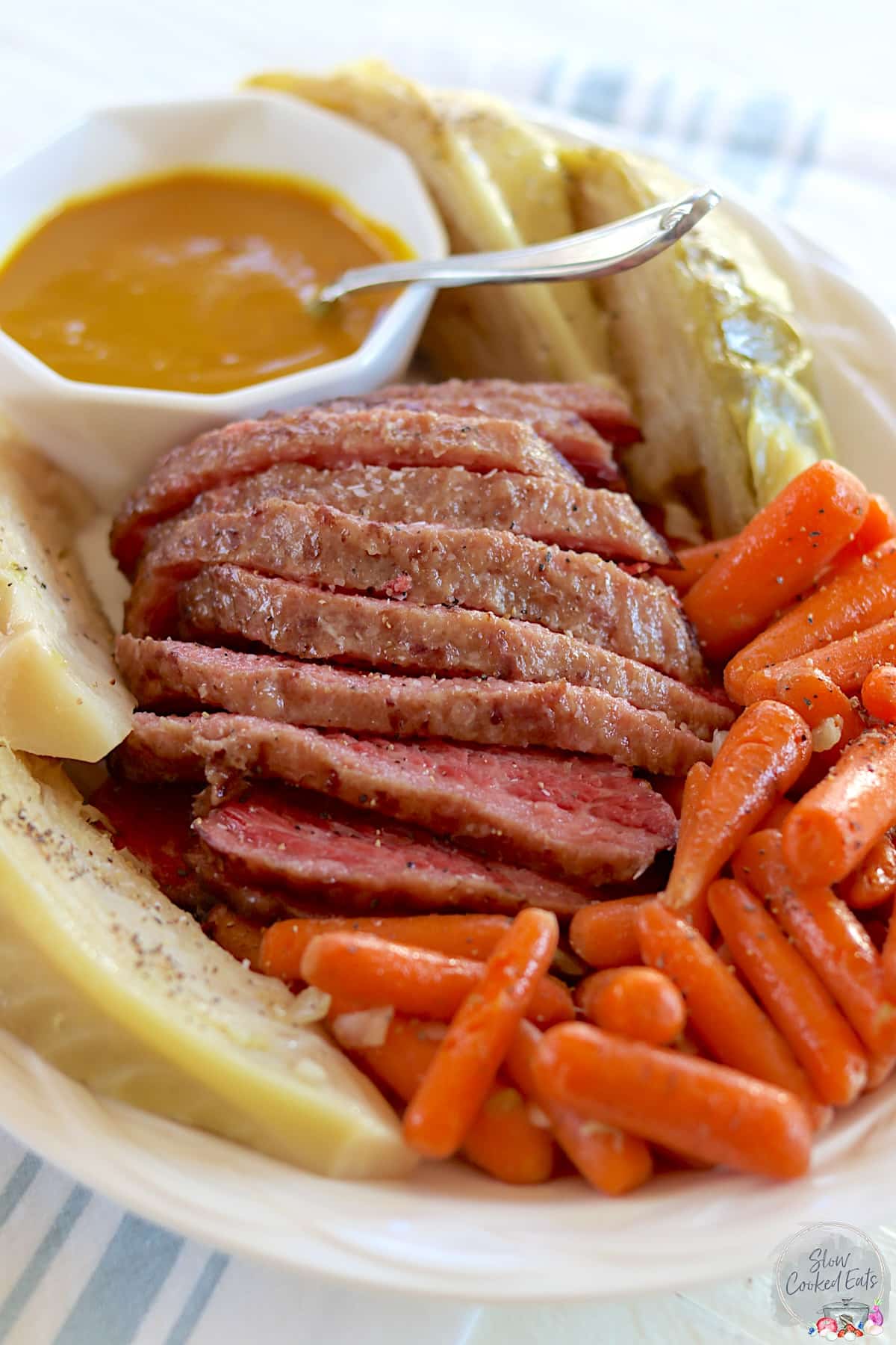 Sliced slow cooker corned beef and cabbage with carrots and mustard sauce on a white platter.