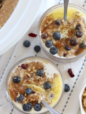 Two clear handles bowls with slow cooker steel cut oats with fresh blueberries and melting butter and brown sugar.