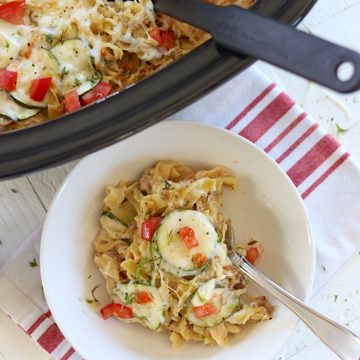 A white bowl of crock pot tuna casserole with sliced zucchini and diced tomatoes.