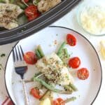 A white plate with green beans and tomatoes with crockpot cod.