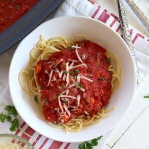 Crock pot marinara sauce served over spaghetti pasta in a white bowl with parmesan cheese.