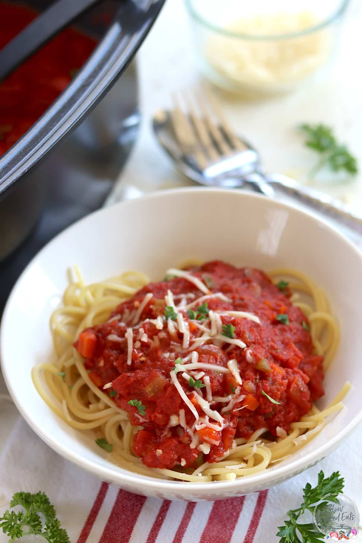 A white bowl of crock pot marinara sauce over spaghetti noodles.