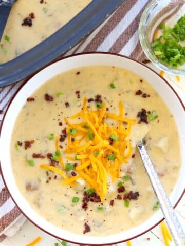 Loaded potato soup in a black oval crockpot with shreded cheddar cheese.