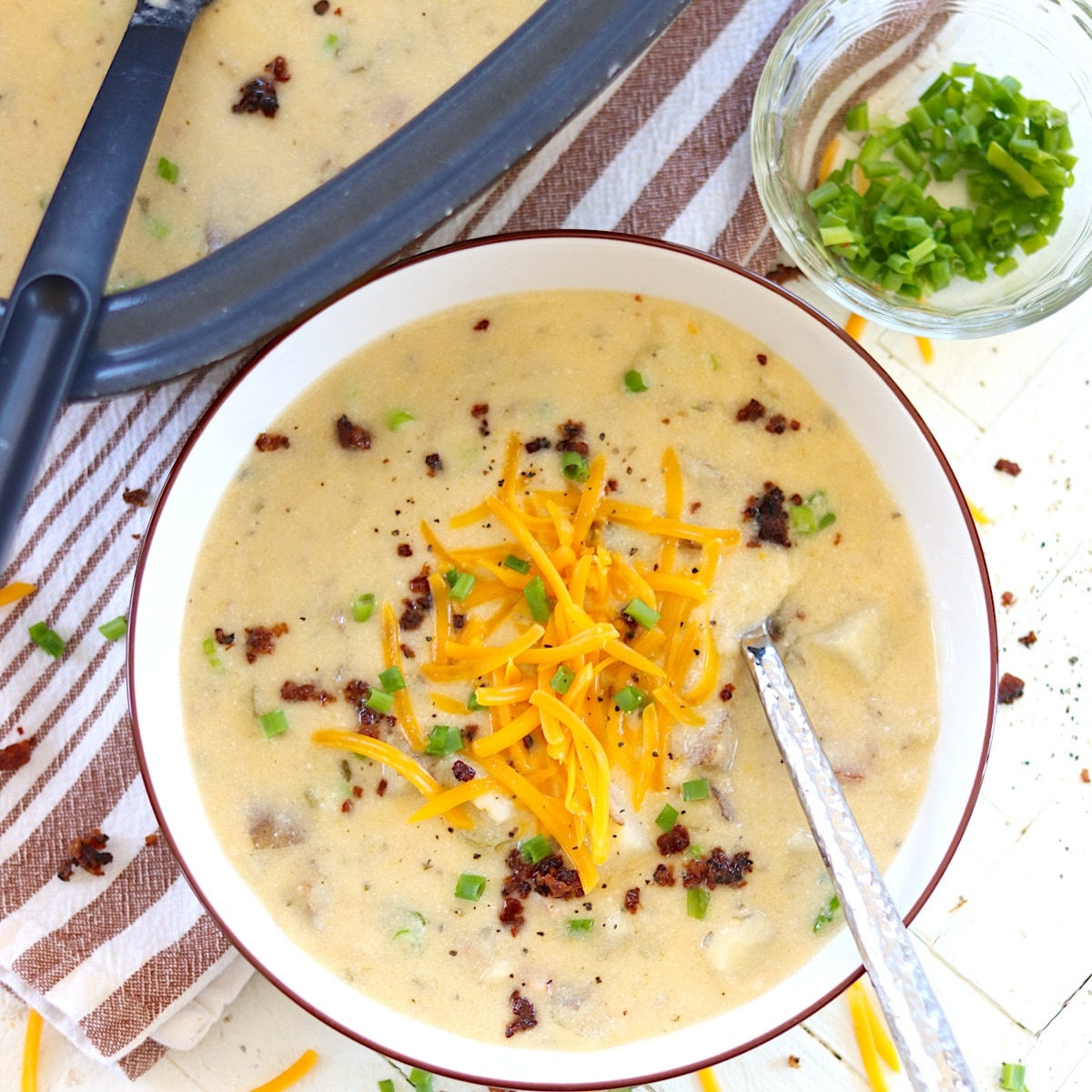 Loaded potato soup in a black oval crockpot with shreded cheddar cheese.