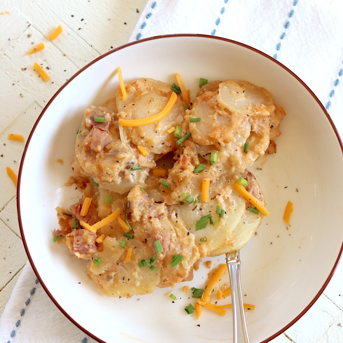 A white bowl of scalloped potatoes and ham in the crockpot.