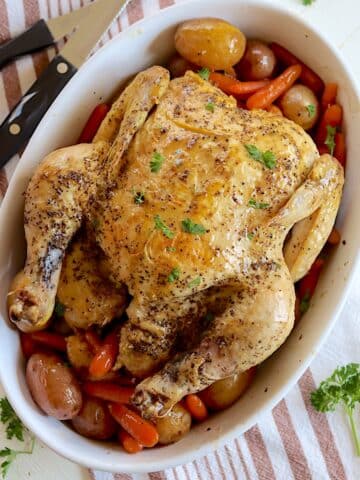 An oval white platter with a slow cooker whole chicken with baby potatoes and carrots.