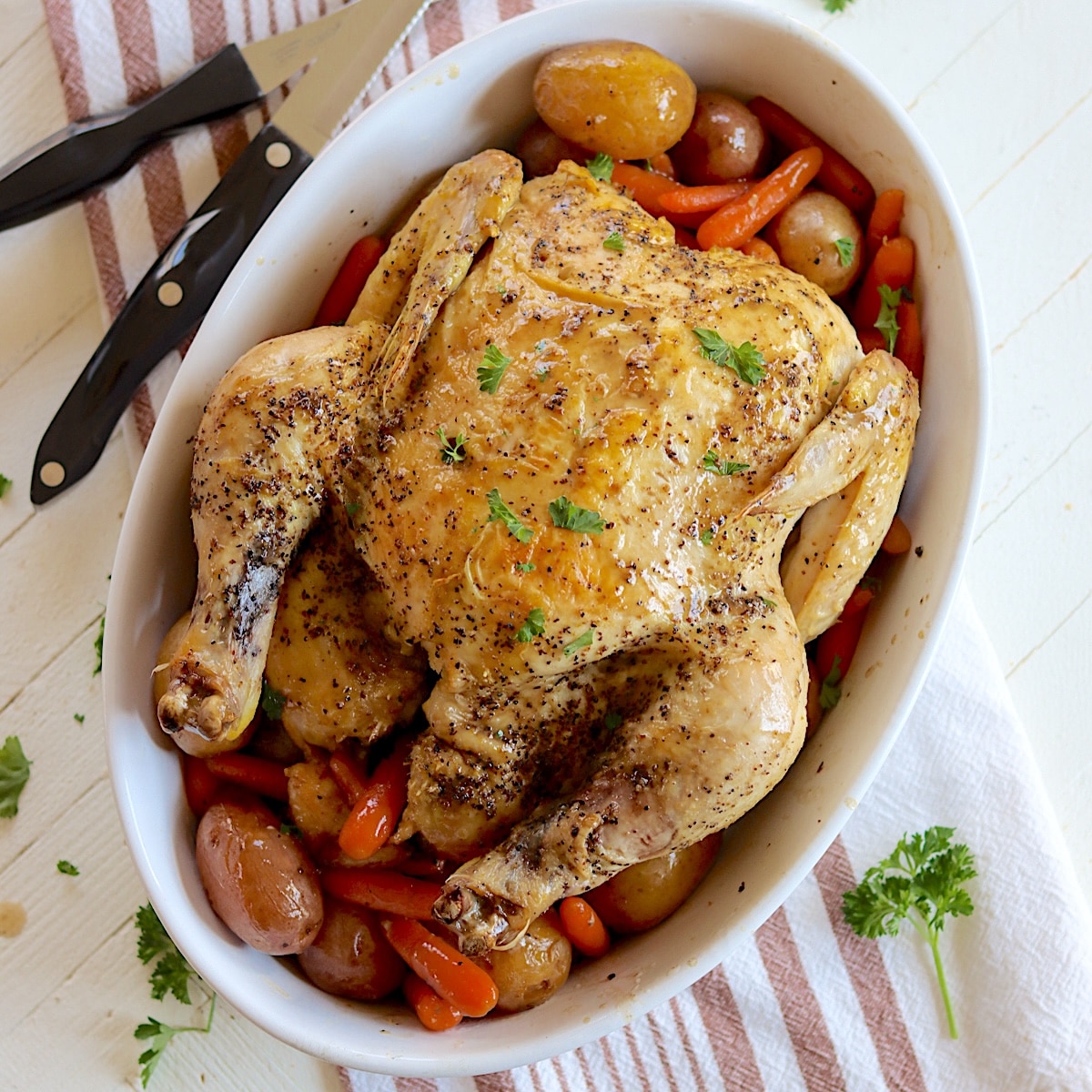 An oval white platter with a slow cooker whole chicken with baby potatoes and carrots.