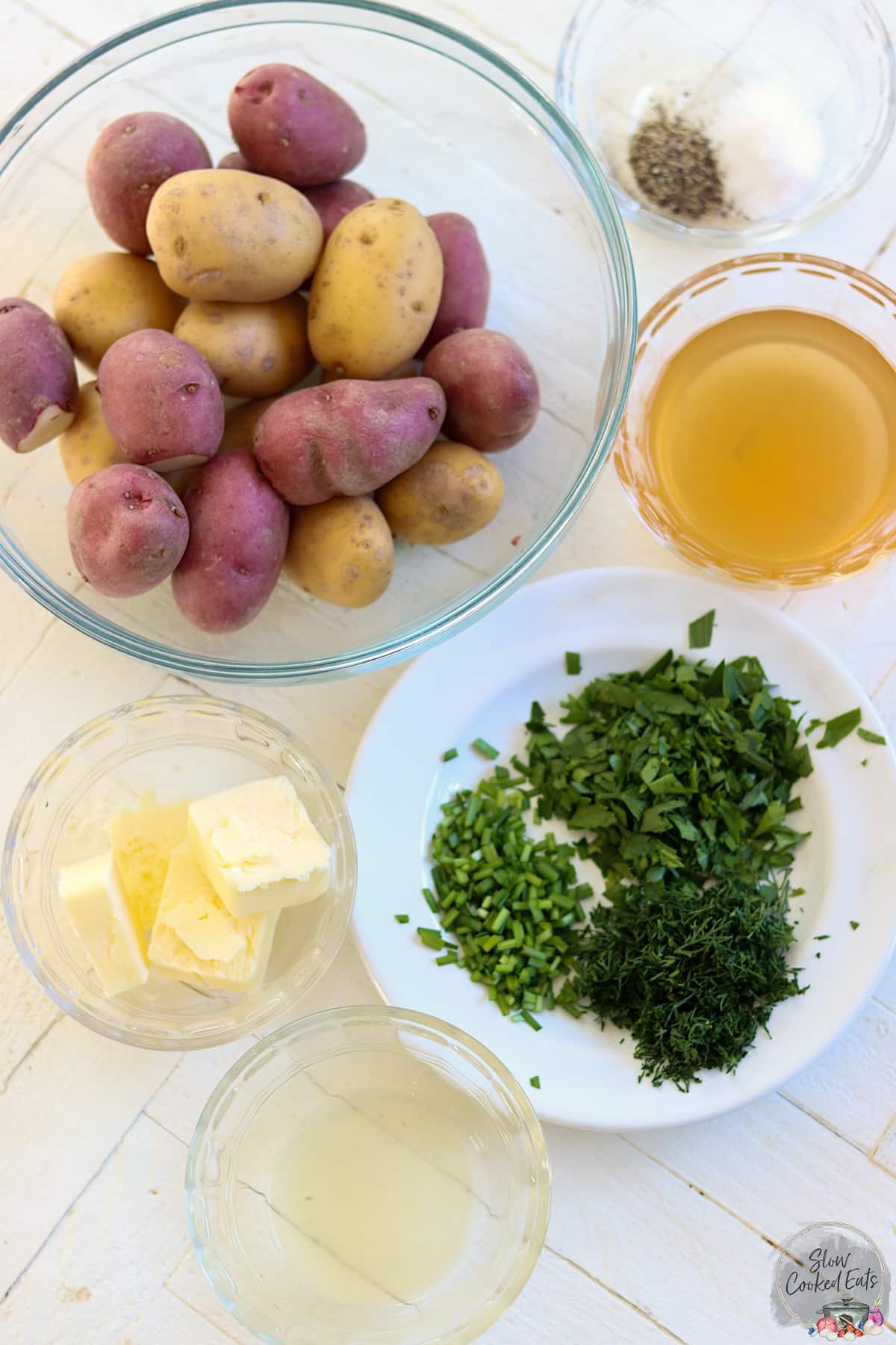 Ingredients needed for making slow cooker baby potatoes on a white wooden board.