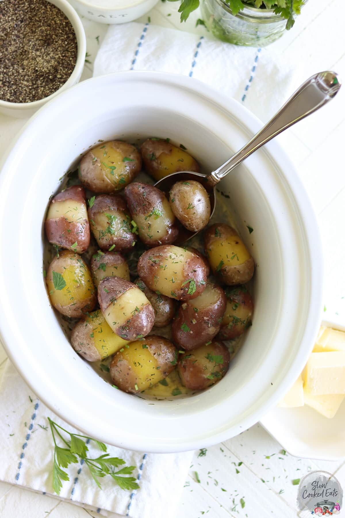 A white oval crockpot of cooked herbed baby potatoes.