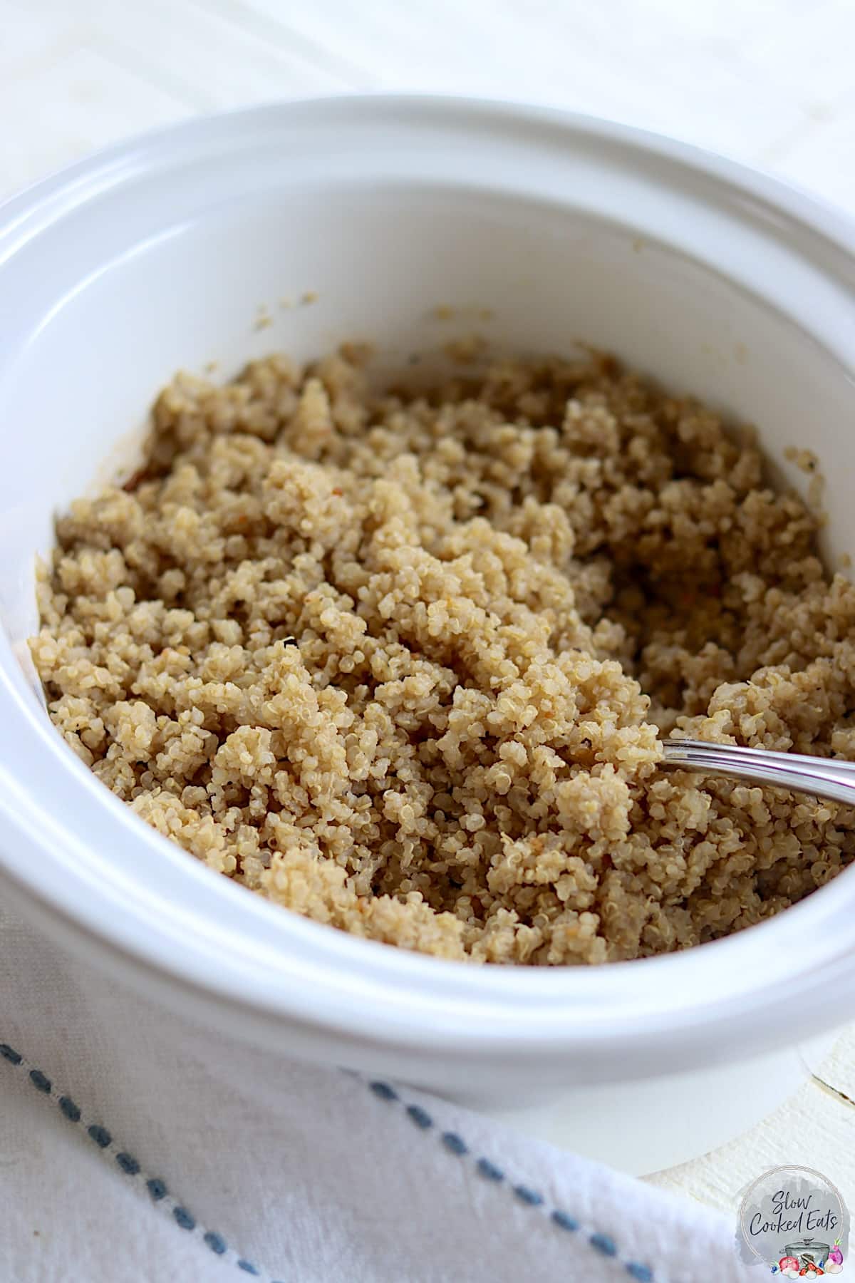 Fully cooked quinoa in slow cooker with a serving spoon.