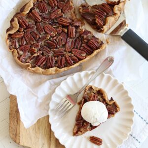 A slice of crockpot peca pie with vanilla ice cream on a scalloped plate.