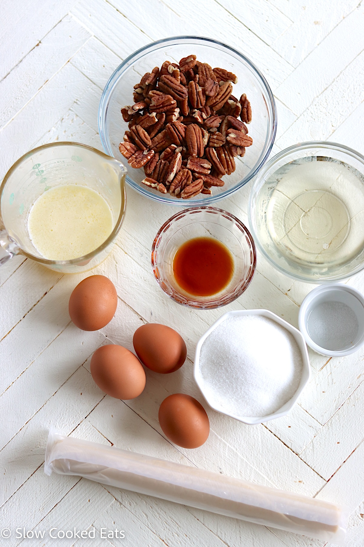 Ingredients needed for making crock pot pecan pie on a white wooden board.